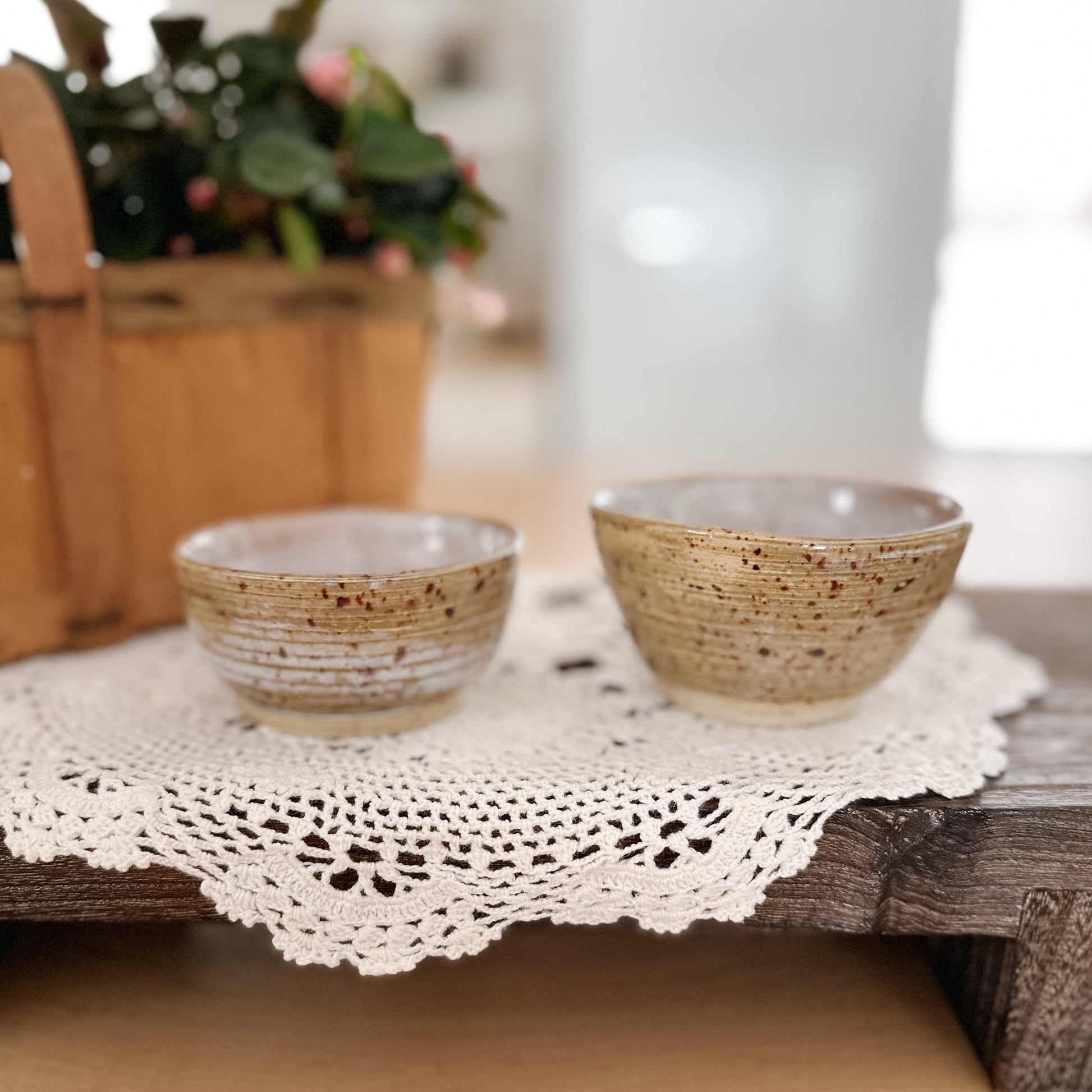 Two ceramic bowls on a wooden surface with a lace doily underneath, blurred background