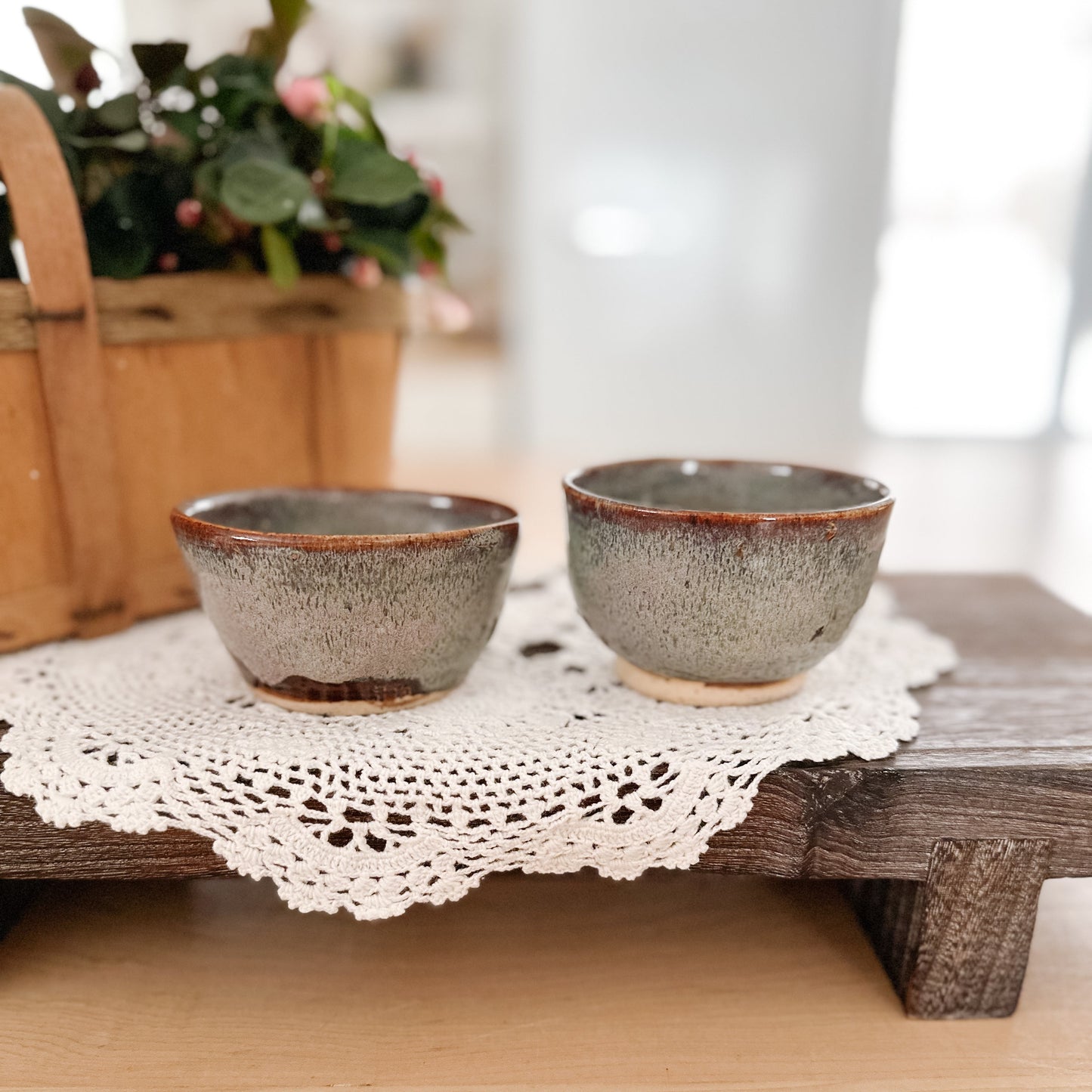 Two ceramic bowls on a wooden stand with a doily underneath, blurred background