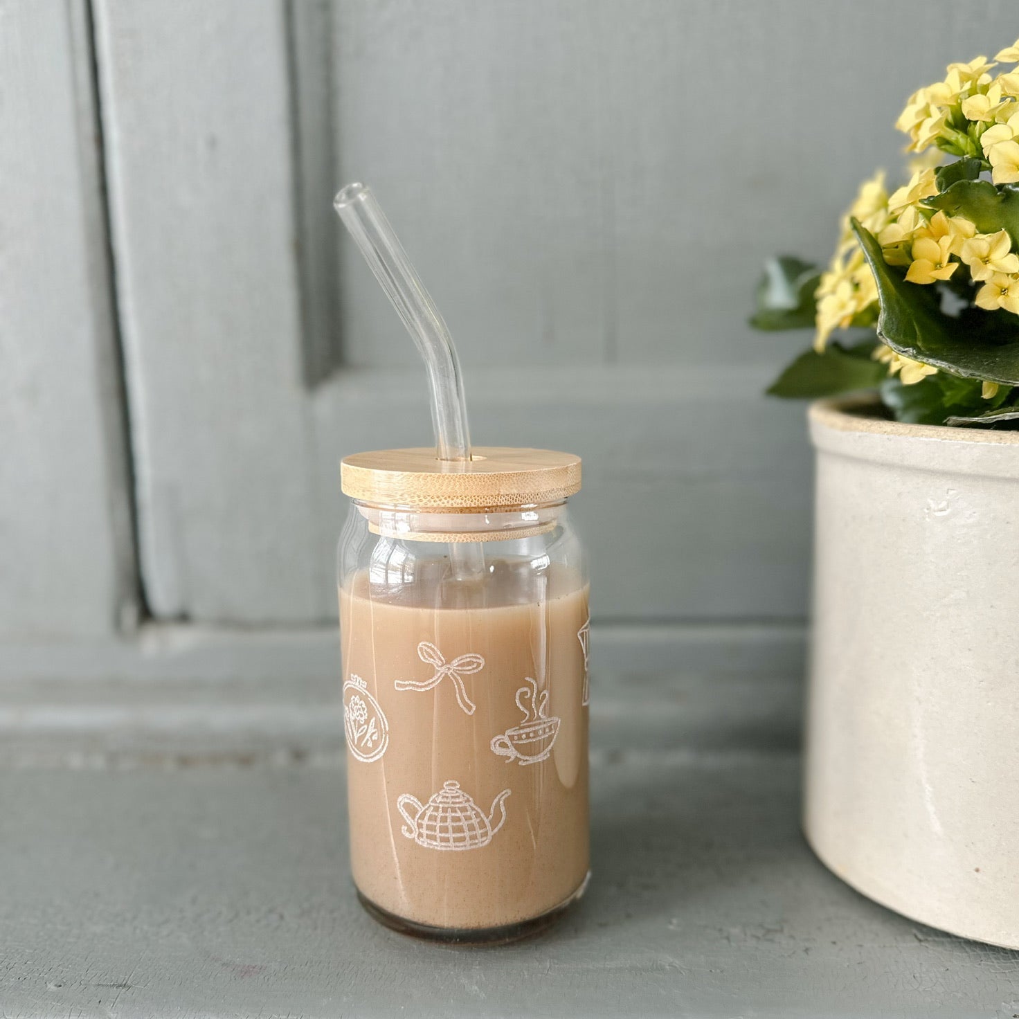 Glass with a wooden lid and straw on a gray surface with a plant in the background