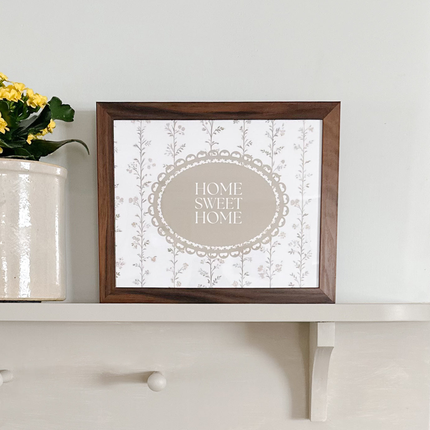 Framed 'Home Sweet Home' print on a shelf with a plant.