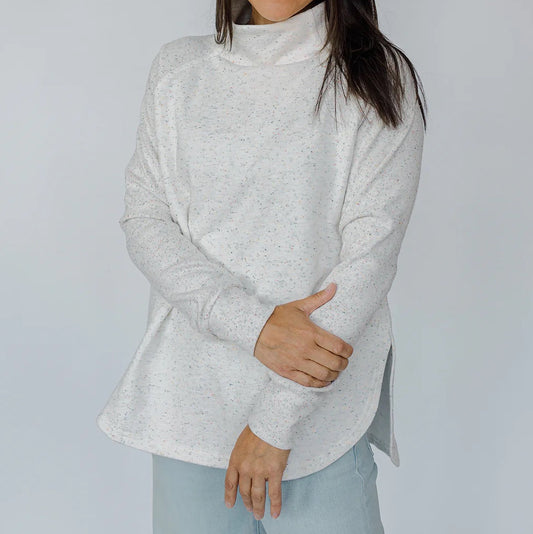 Woman wearing a light gray turtleneck sweater and light blue jeans against a white background