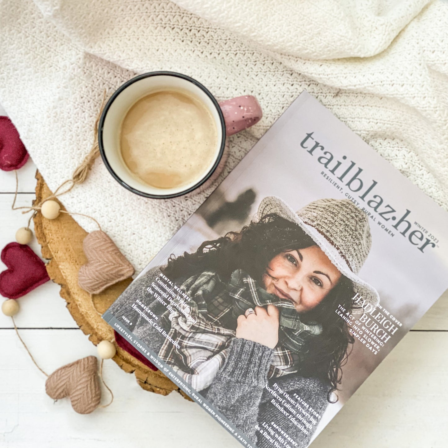 Trailblazer Magazine flat lay next to mug of coffee and garland with hearts