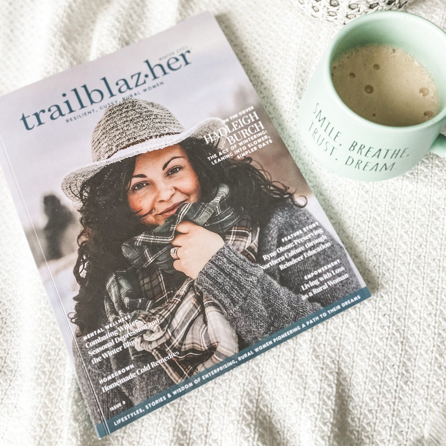 Trailblazher magazine flatlay next to green coffee mug with quote "smile, breathe, trust, dream"
